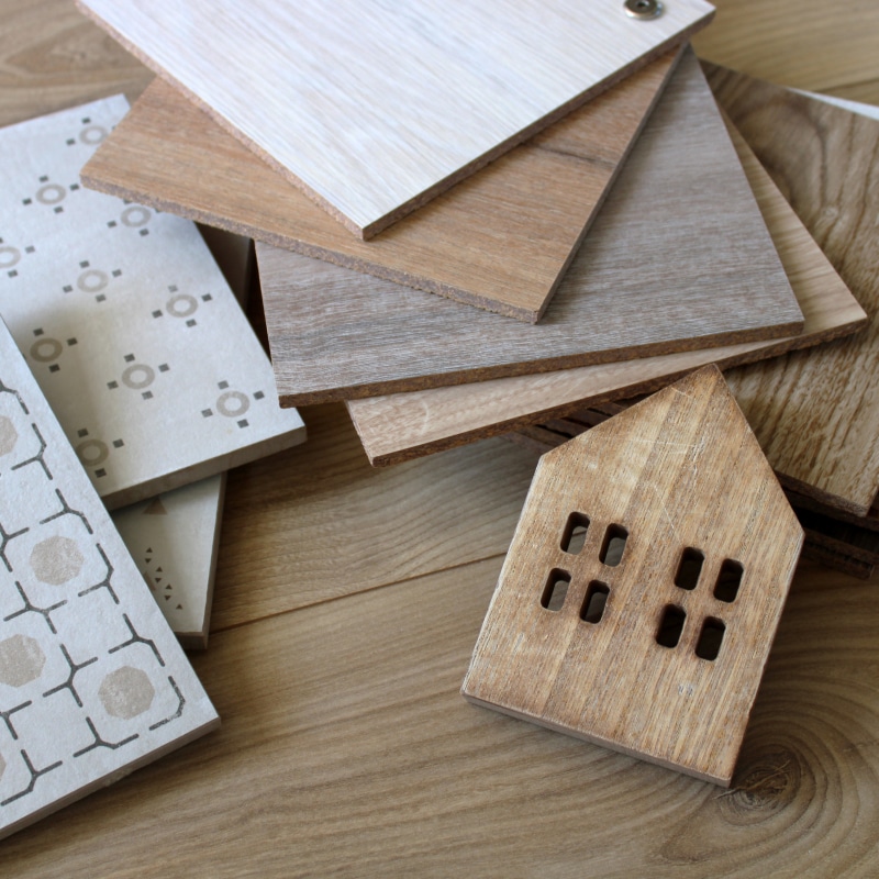 Sélection d'échantillons de parquets en bois et carreaux de ciment avec une petite maison décorative en bois.