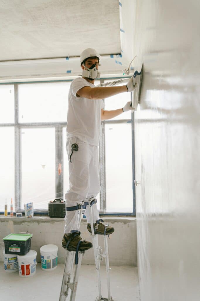 Construction worker smoothing a wall indoors using safety gear.