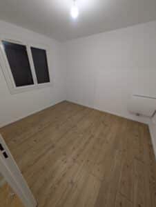 Pièce vide fraîchement rénovée. Murs blancs, sol en parquet imitation bois rustique, grande fenêtre et radiateur électrique mural.