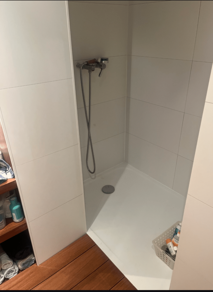 Douche italienne moderne avec carrelage blanc, receveur extra-plat et caillebotis en bois chaleureux.