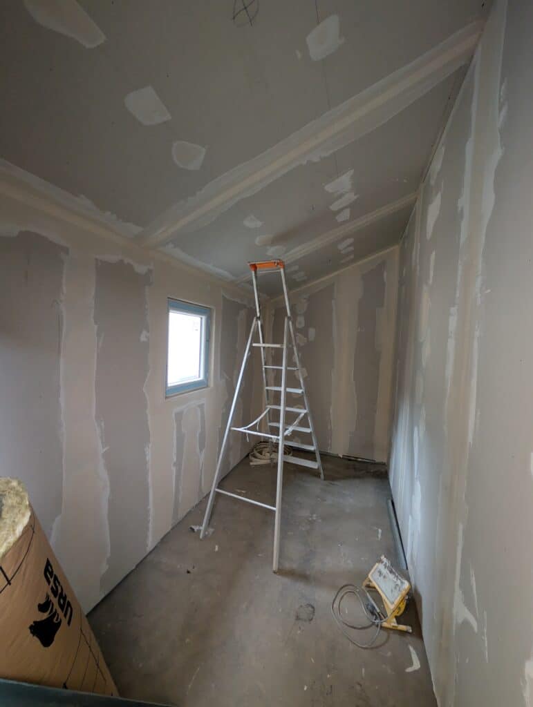 Intérieur en travaux avec plaques de plâtre jointoyées, escabeau, fenêtre et isolant URSA sur sol en béton.